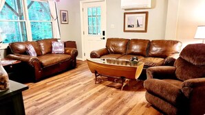 A living room with two brown leather sofas, a wooden coffee table, and a small boat model. - Spacious suite surrounded by nature with living room, fireplace, porch, fire pit (Blowing Rock)
