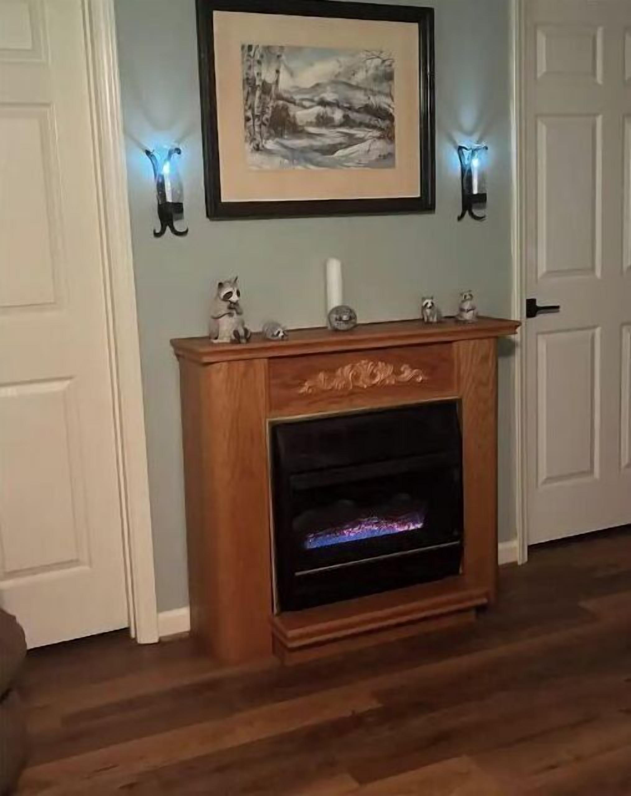 Una chimenea encendida, flanqueada por dos apliques de pared y un cuadro de paisaje colgado encima.