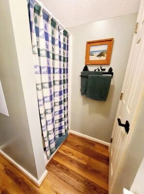 A hallway with a wooden floor, featuring a partially open door and a framed picture on the wall.