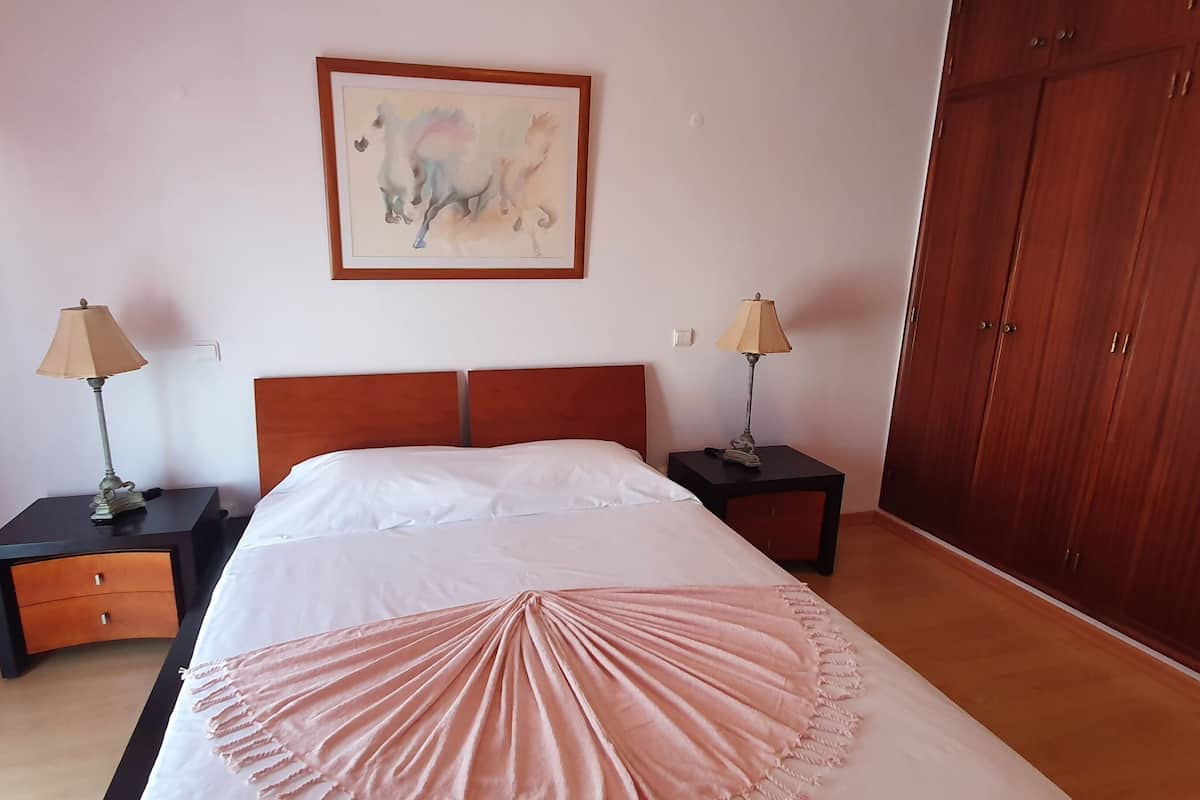 A bedroom with a bed, two nightstands, a lamp, a wardrobe, and a painting on the wall.