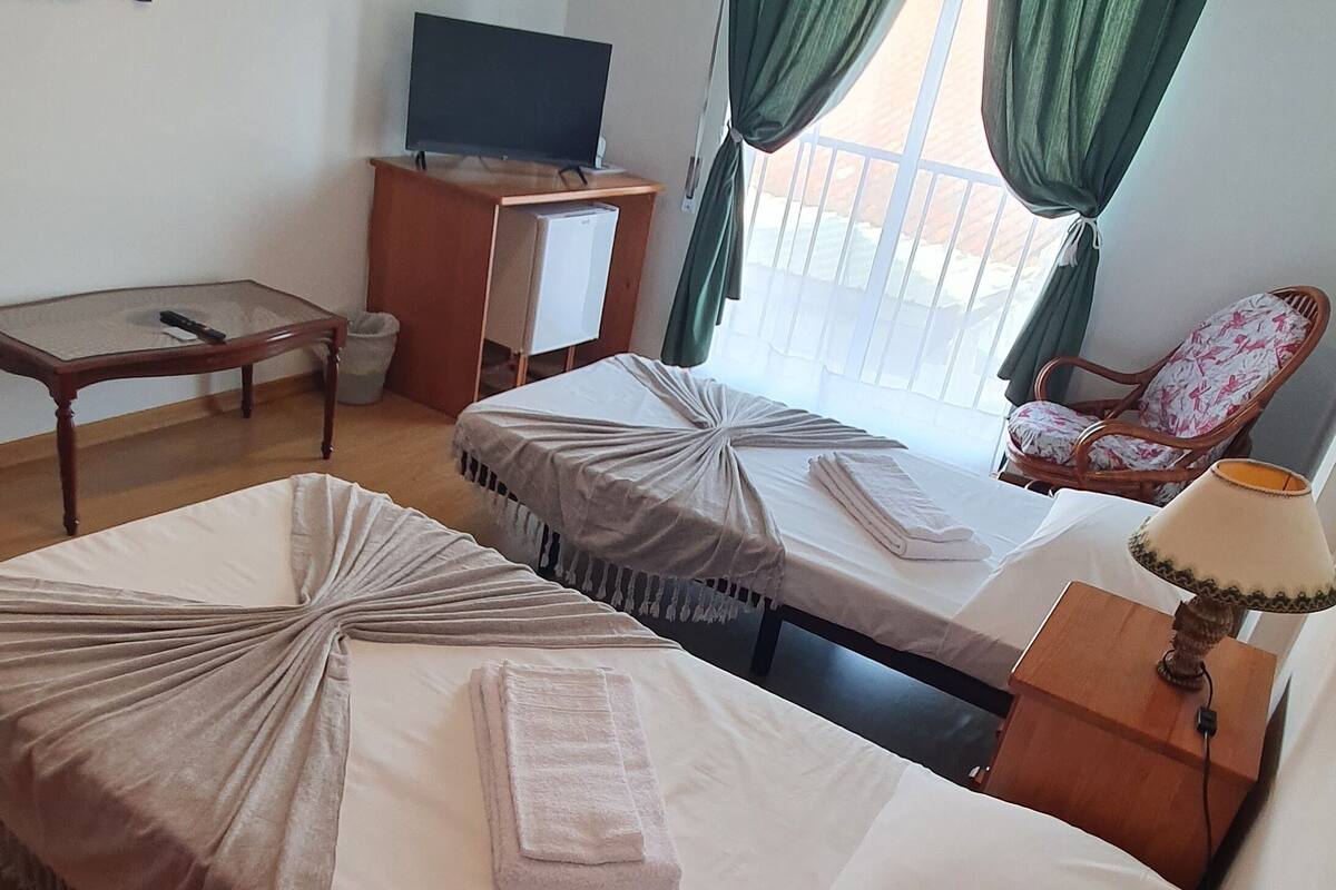 A hotel room with two beds, a television, a table, and a chair.
