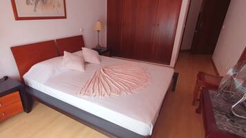 Un letto rifatto con cura, una coperta decorativa rosa, un comodino in legno con una lampada e un armadio in una camera d'albergo.