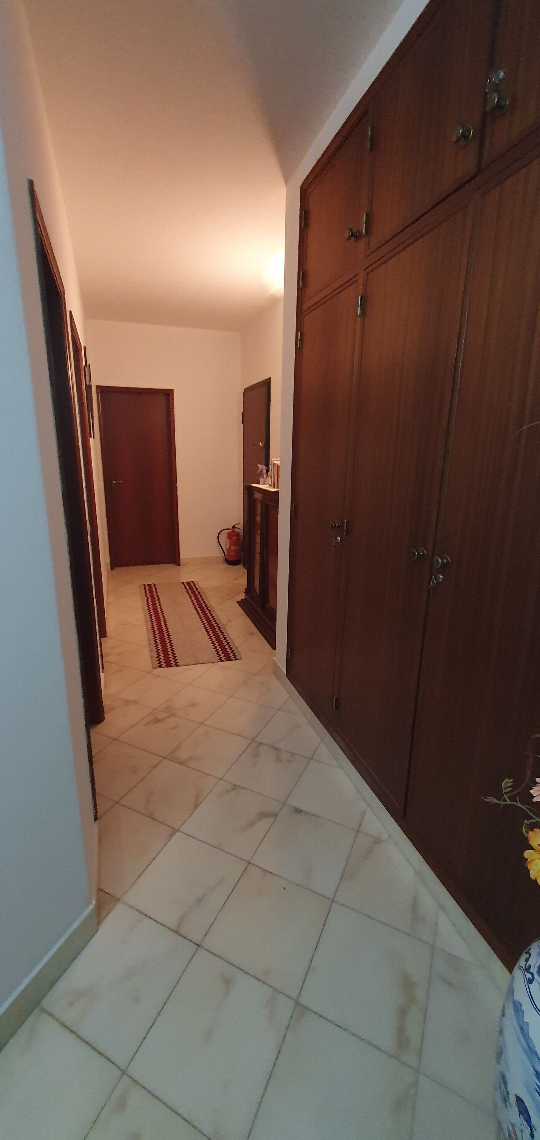 Un pasillo con suelo de baldosas, un armario de madera y una puerta al final.