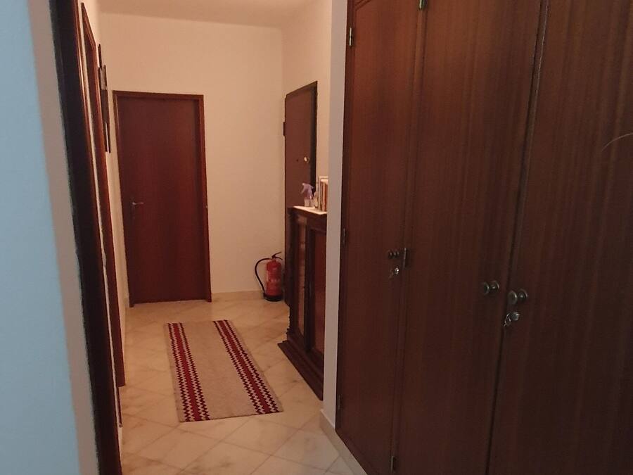 Un pasillo con suelo de baldosas, un armario de madera y una puerta al final.