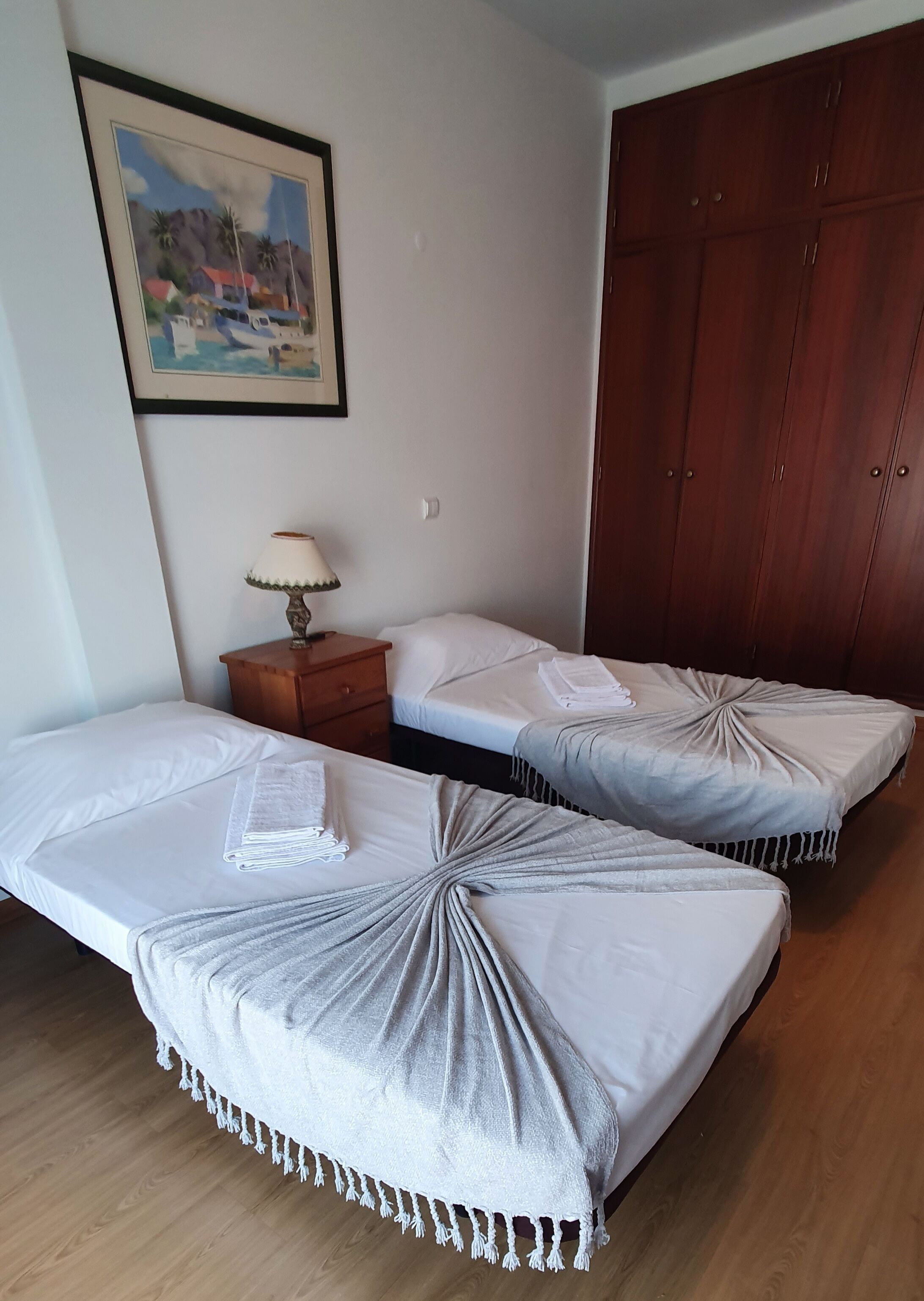 Une chambre d’hôtel avec deux lits simples, une armoire en bois, une table de chevet avec une lampe et un tableau encadré au mur.
