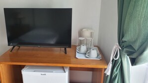 Un meuble en bois pour la télévision, sur lequel est posé un téléviseur à écran plat, un petit réfrigérateur blanc et un plateau avec deux tasses blanches et un verre.