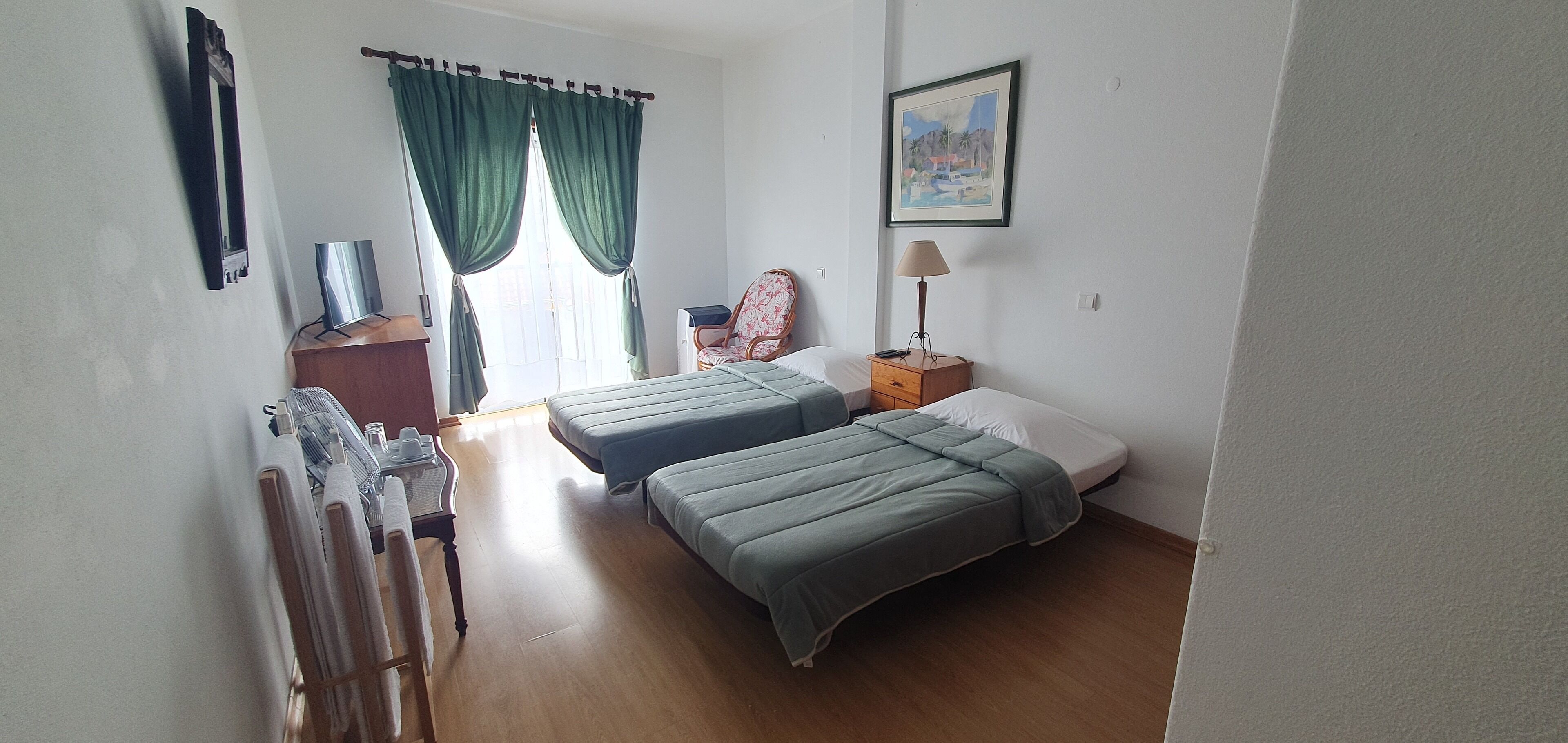 A room with two beds, a chair, a desk, a lamp, and a painting on the wall.