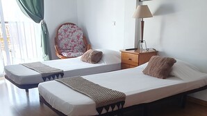 Une chambre avec deux lits simples, une chaise, une petite table, une lampe et un tableau au mur.
