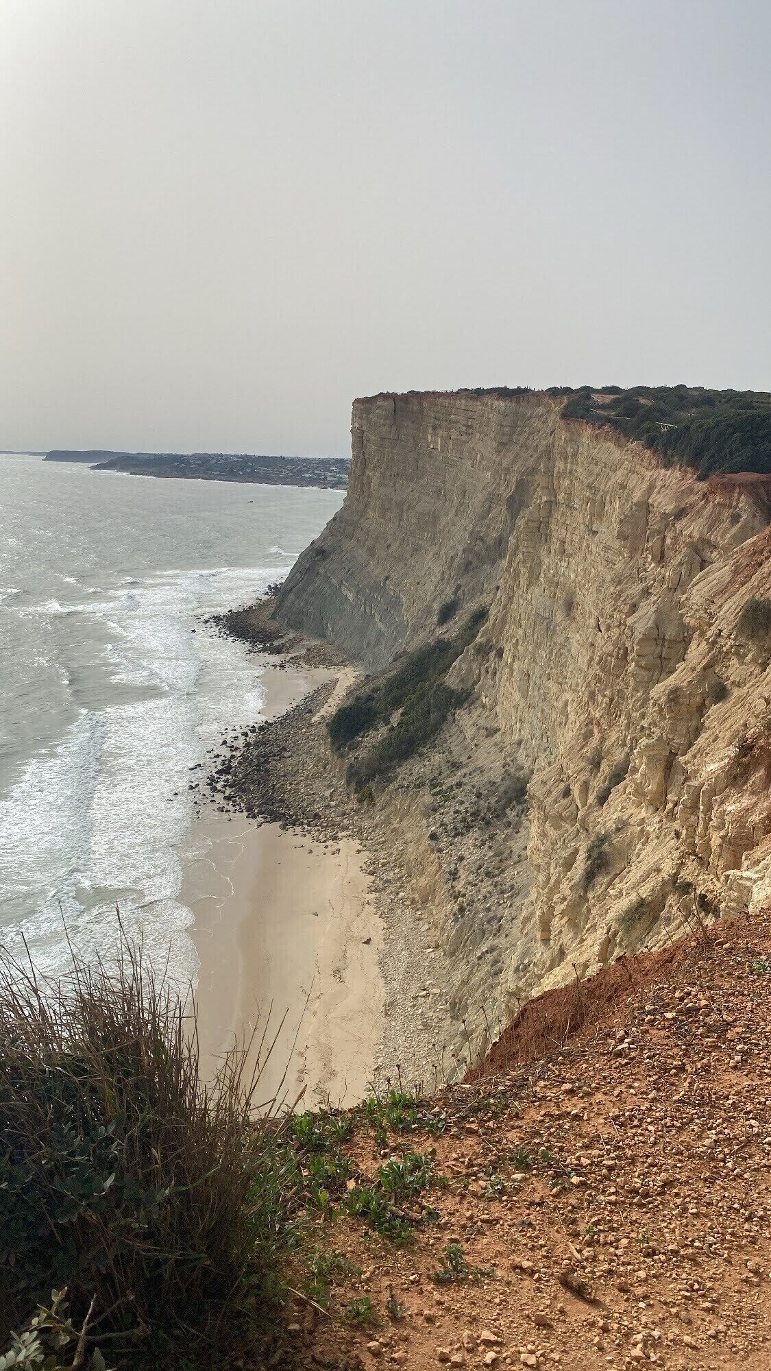 Un paysage côtier caractérisé par une falaise abrupte, une plage de sable et des vagues de l’océan.