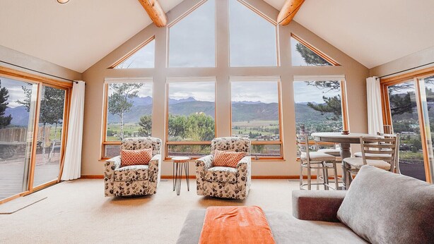 A spacious room with large windows offering mountain views, a wooden ceiling, and a cozy seating area with a table and chairs. - Beautiful 30+ Stay | Amazing Views | Large Deck | Air Conditioning (Ridgway)