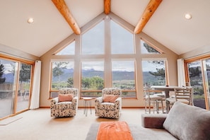 A spacious room with large windows offering mountain views, a wooden ceiling, and a cozy seating area with a table and chairs. - Beautiful 30+ Stay | Amazing Views | Large Deck | Air Conditioning (Ridgway)