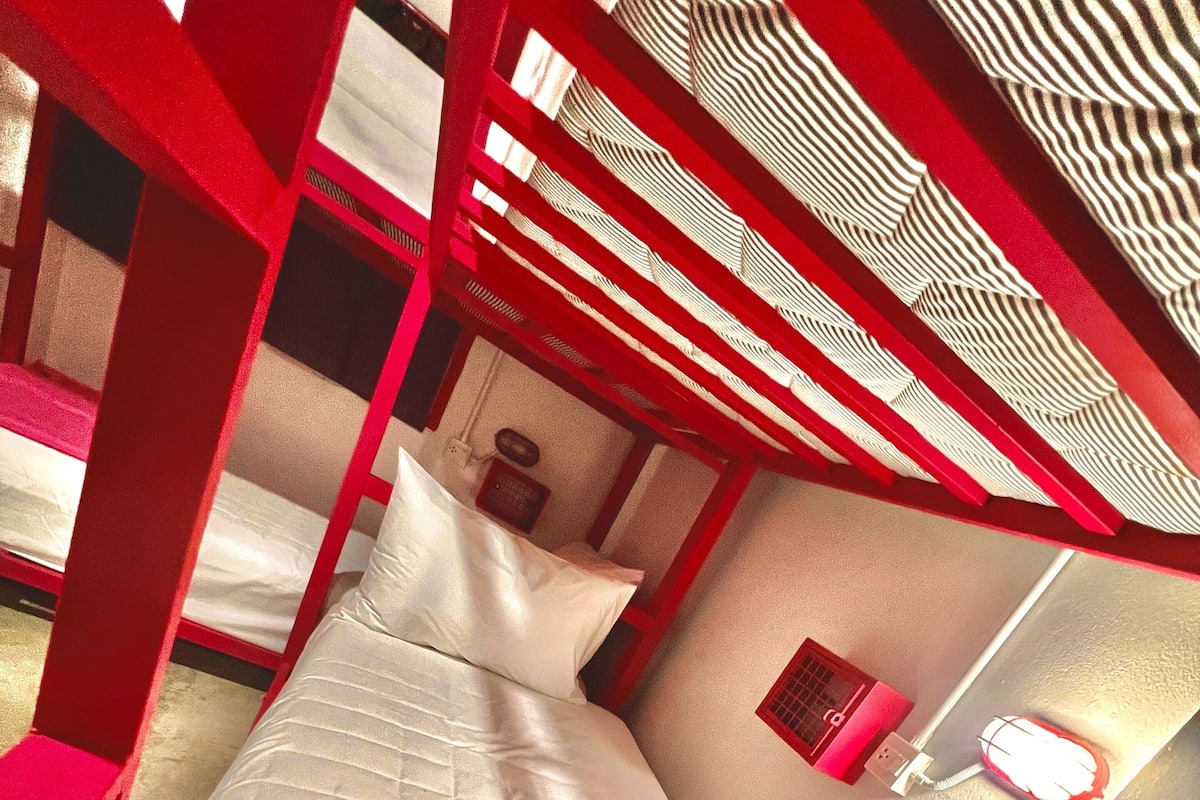 Une chambre avec un lit superposé, dont la structure est rouge, le matelas blanc et la couverture rouge.