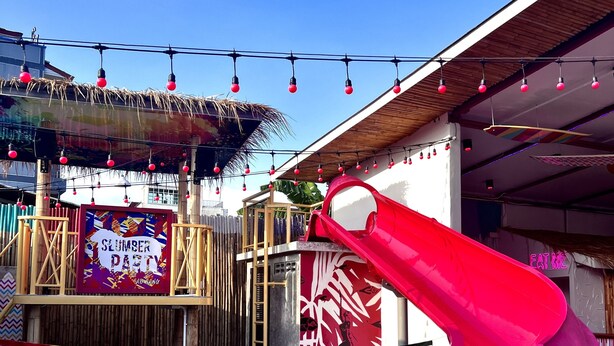 A pool area with a water slide, a sign reading "SLUMBER PARTY", and a tropical-themed mural. - Slumber Party Krabi  (Krabi)