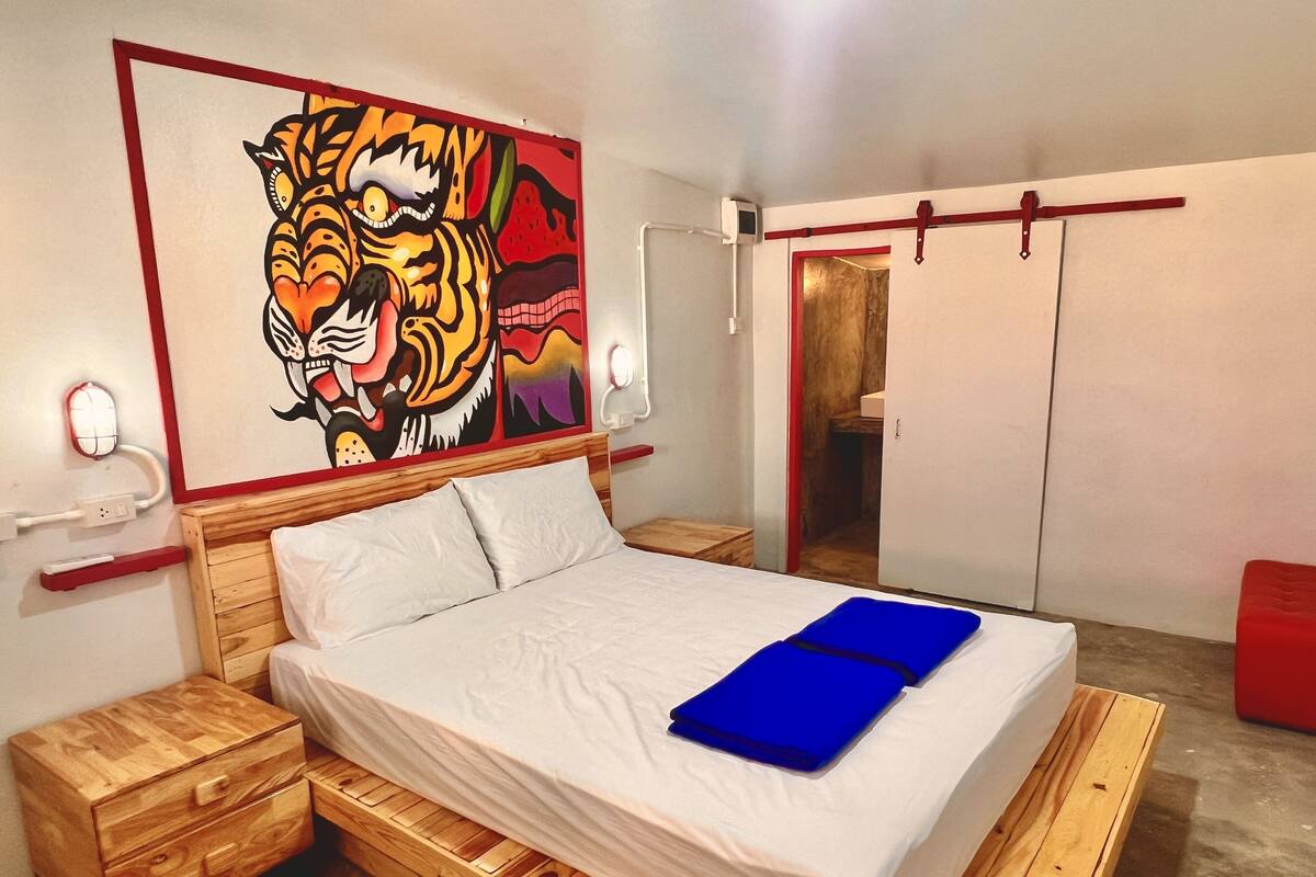 Une chambre avec un lit en bois, un tableau coloré représentant un tigre accroché au mur, un banc rouge et une armoire.
