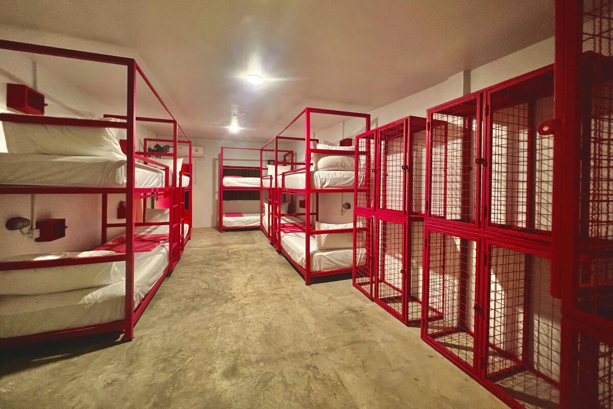 Un couloir bordé de lits superposés, disposés par paires de chaque côté, qui mène à une pièce comprenant un lit et une fenêtre.