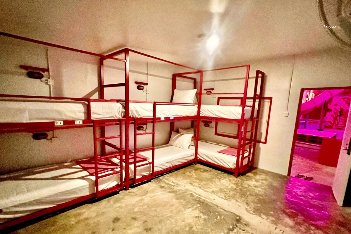 Une chambre avec trois lits superposés, une petite fenêtre et une porte donnant sur une autre pièce.