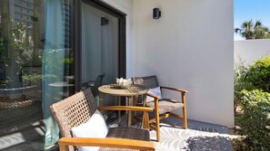 Un pequeño espacio al aire libre con mobiliario de mimbre y un ventanal de vidrio que da a un balcón.