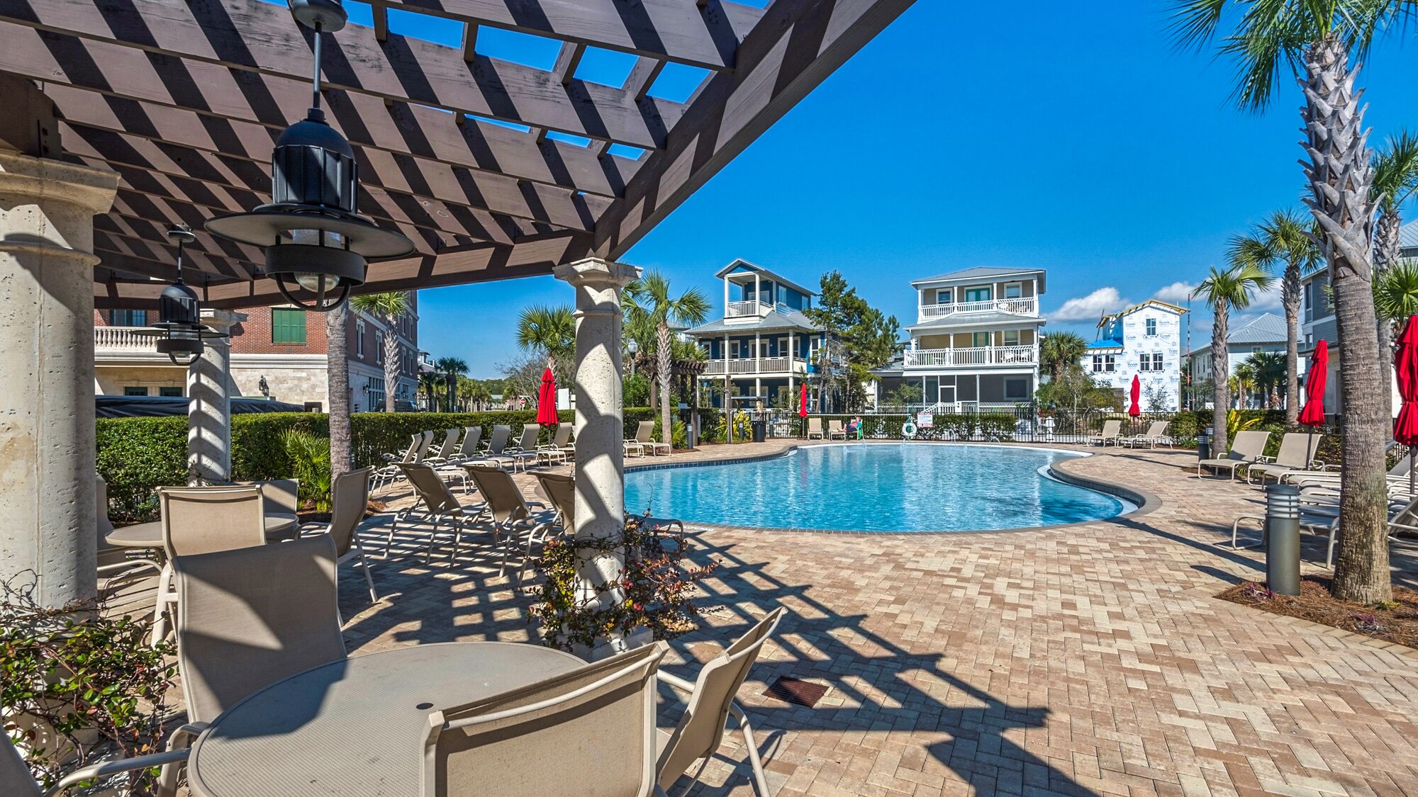 A poolside area with lounge chairs and umbrellas, a clear blue pool, and buildings in the background.