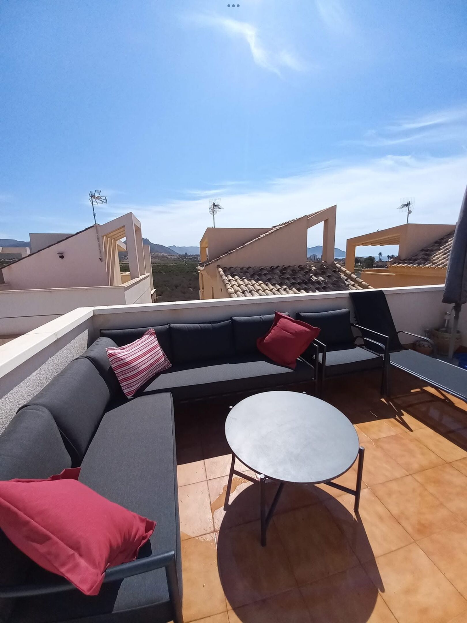 A rooftop terrace with a sectional sofa, a round table, and a view of the city and mountains in the background.