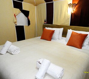 A hotel room with a bed, pillows, a rolled towel, and a wall-mounted light fixture.