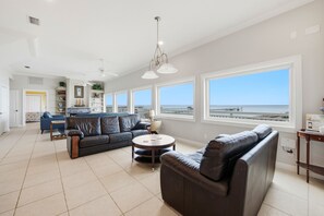 A spacious living area with a large window overlooking the sea, a black leather sofa, a coffee table, and a blue armchair. - Welcome to La Vista! (St. George Island)