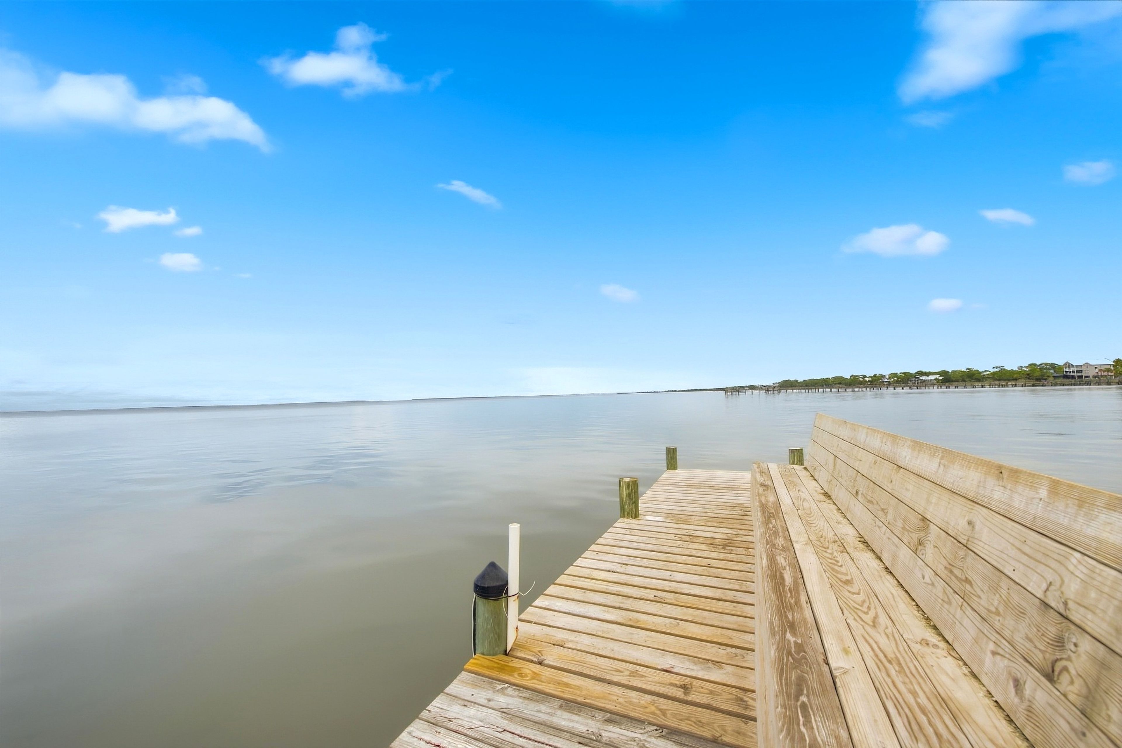 A wooden pier extending into calm water with a clear sky above.