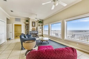 A spacious living room with a large window overlooking a pier, a ceiling fan, and a fireplace.