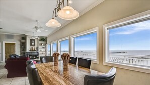 A spacious dining area with a large wooden table, multiple chairs, and large windows offering a view of the ocean and pier. - Welcome to La Vista! (St. George Island)