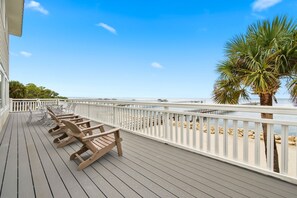 A wooden deck with lounge chairs and a railing overlooking a beach.