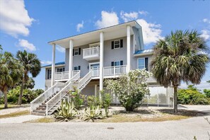 A two-story beachfront house with a balcony, a staircase, and a palm tree in the foreground. - Welcome to La Vista! (St. George Island)
