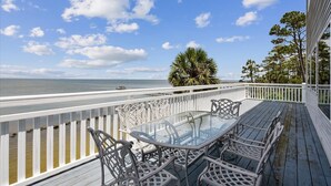 A balcony with a glass table and chairs, overlooking a body of water and a clear sky. - Welcome to La Vista! (St. George Island)