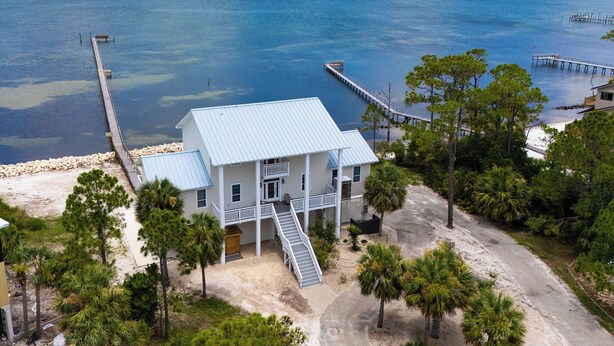 A coastal house with a metal roof, a front porch, and a staircase leading to the entrance. - Welcome to La Vista! (St. George Island)
