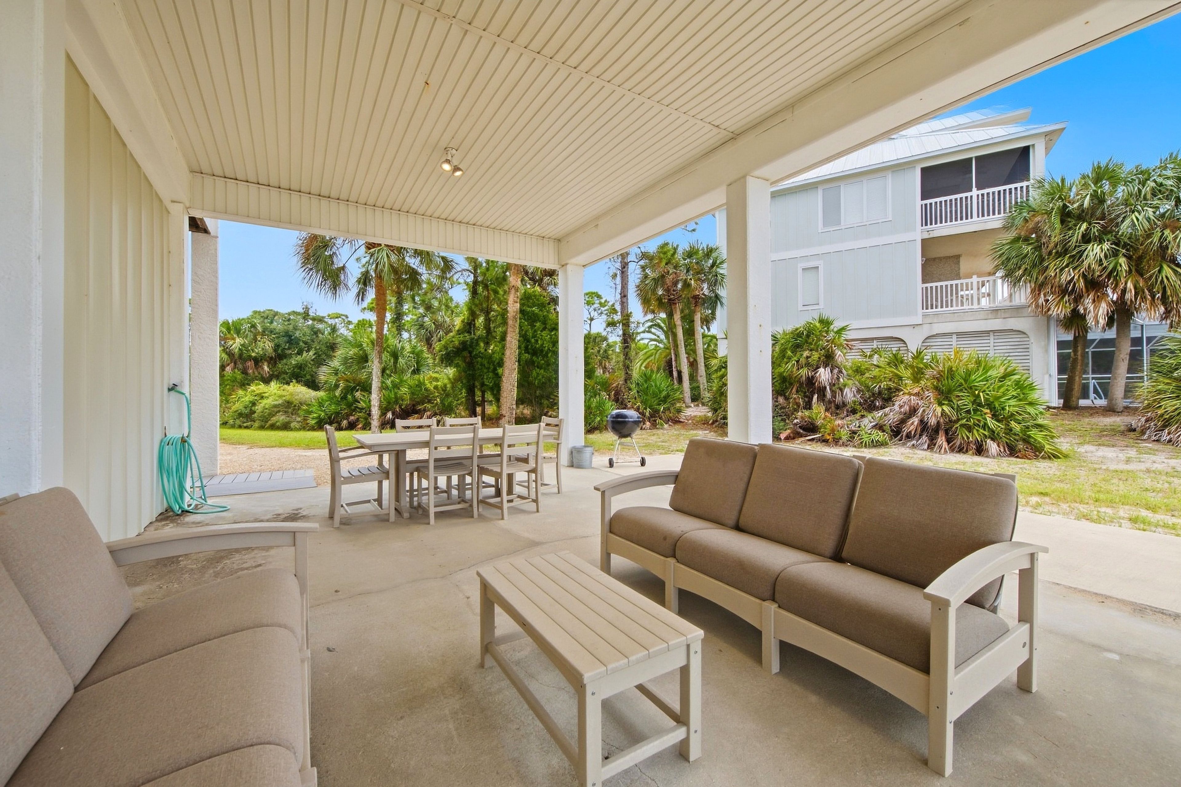 A covered outdoor seating area with a table and chairs, a sofa, and a grill.
