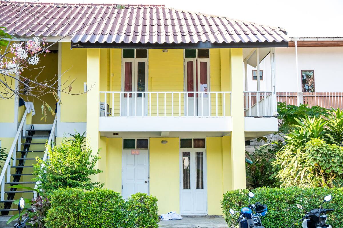 A two-story building with a yellow facade, white balcony railings, and a red-tiled roof.