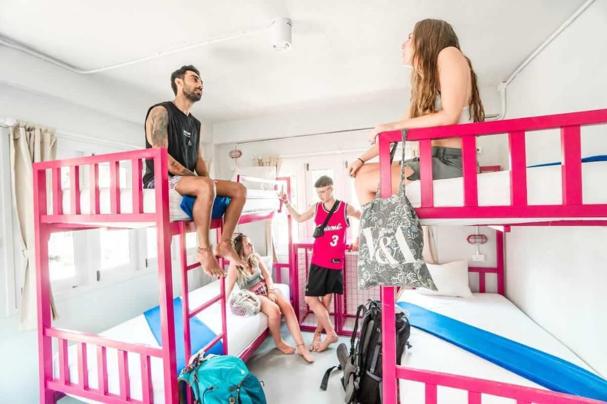 Bunk beds with pink railings, a window with curtains, and a backpack on the floor.