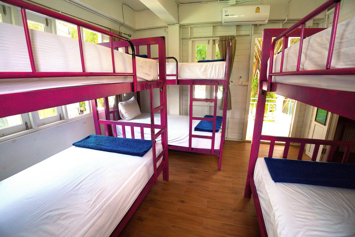 A room with bunk beds, wooden flooring, and a window with curtains.