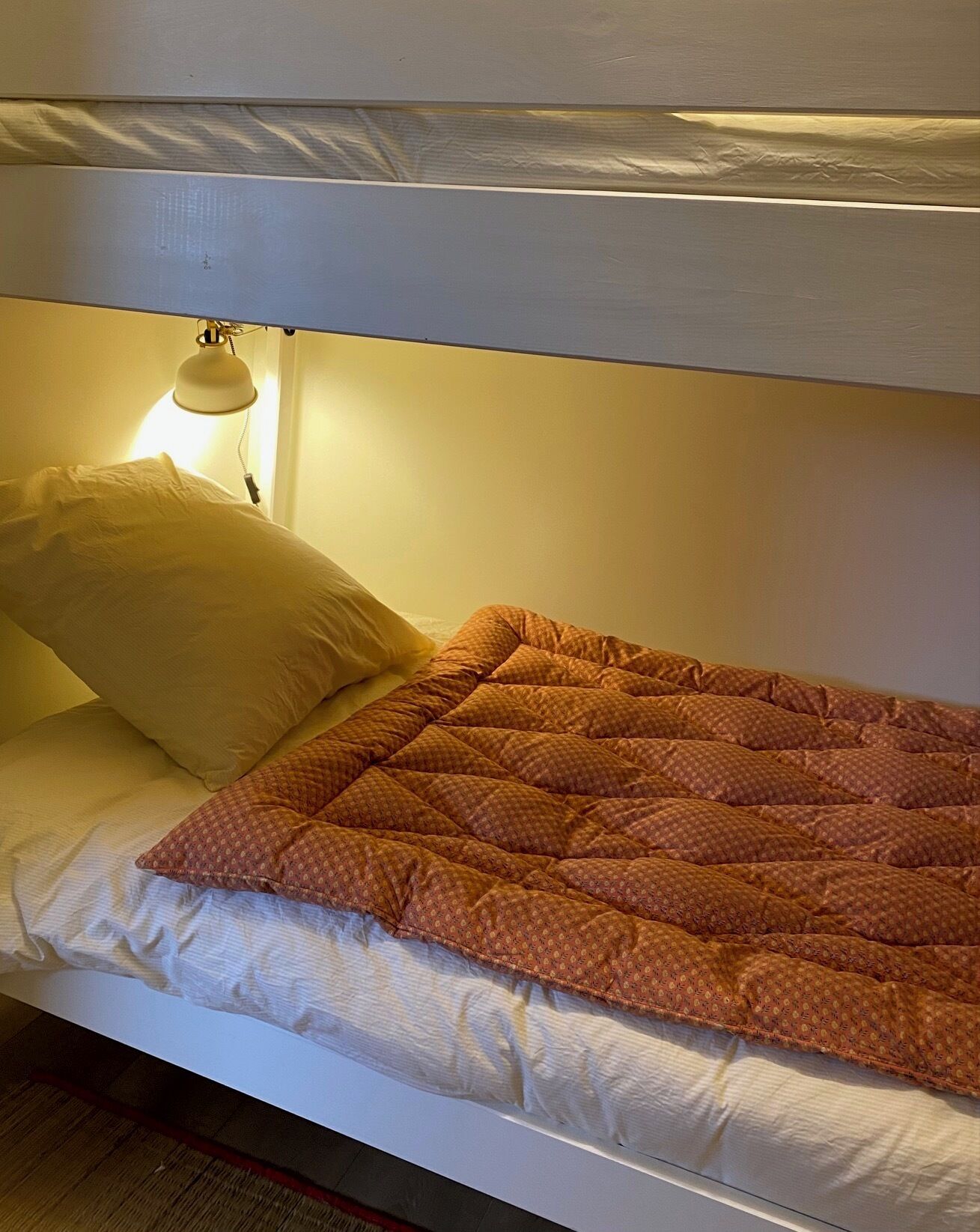 Un lit superposé avec un lit simple en haut et un lit en bas. Une lampe est placée sur le côté du lit du bas.