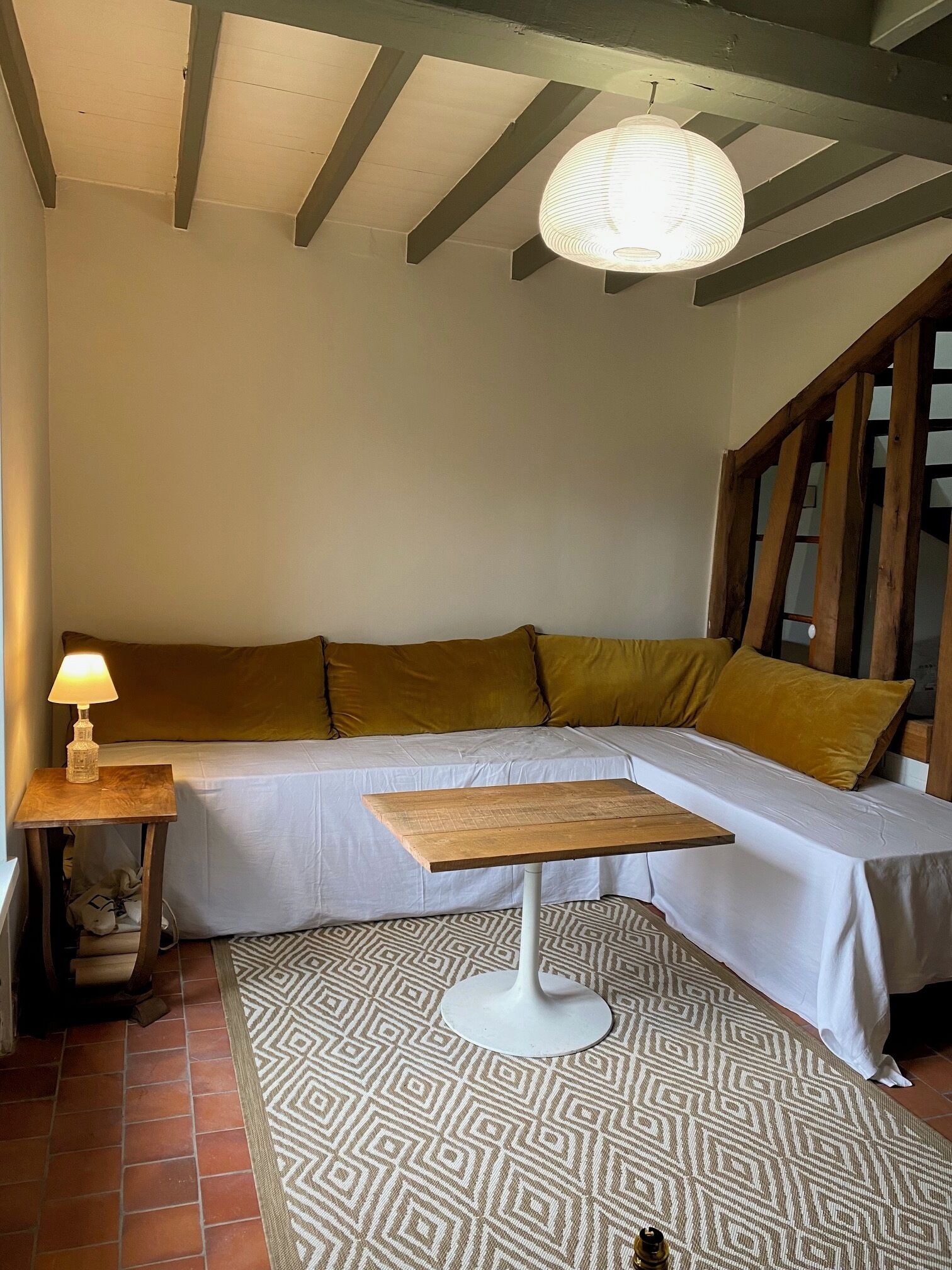 Una habitación acogedora con sofá modular, una mesita de madera, alfombra estampada y lámpara colgante.