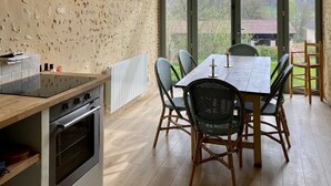 A kitchen with a large window, wooden ceiling beams, and a dining area with wicker chairs.