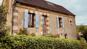 An old, weathered building with a tiled roof and blue shutters.