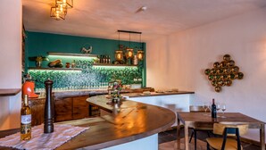 Una cocina moderna con salpicadero verde azulado, barra de bar de madera y zona de comedor con mesa y sillas de madera.