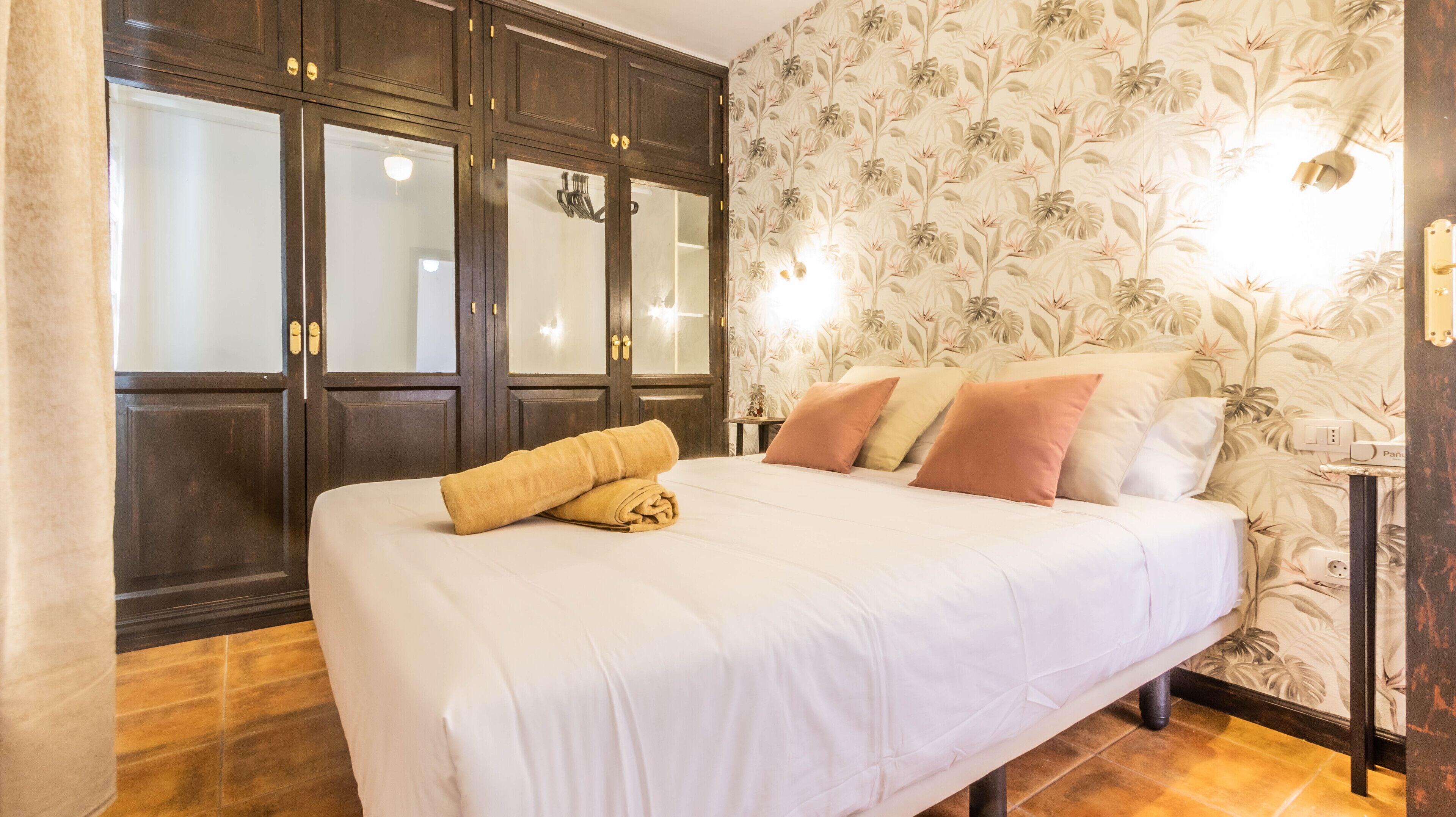 A hotel room with a large bed, a wardrobe, and a floral wallpaper.