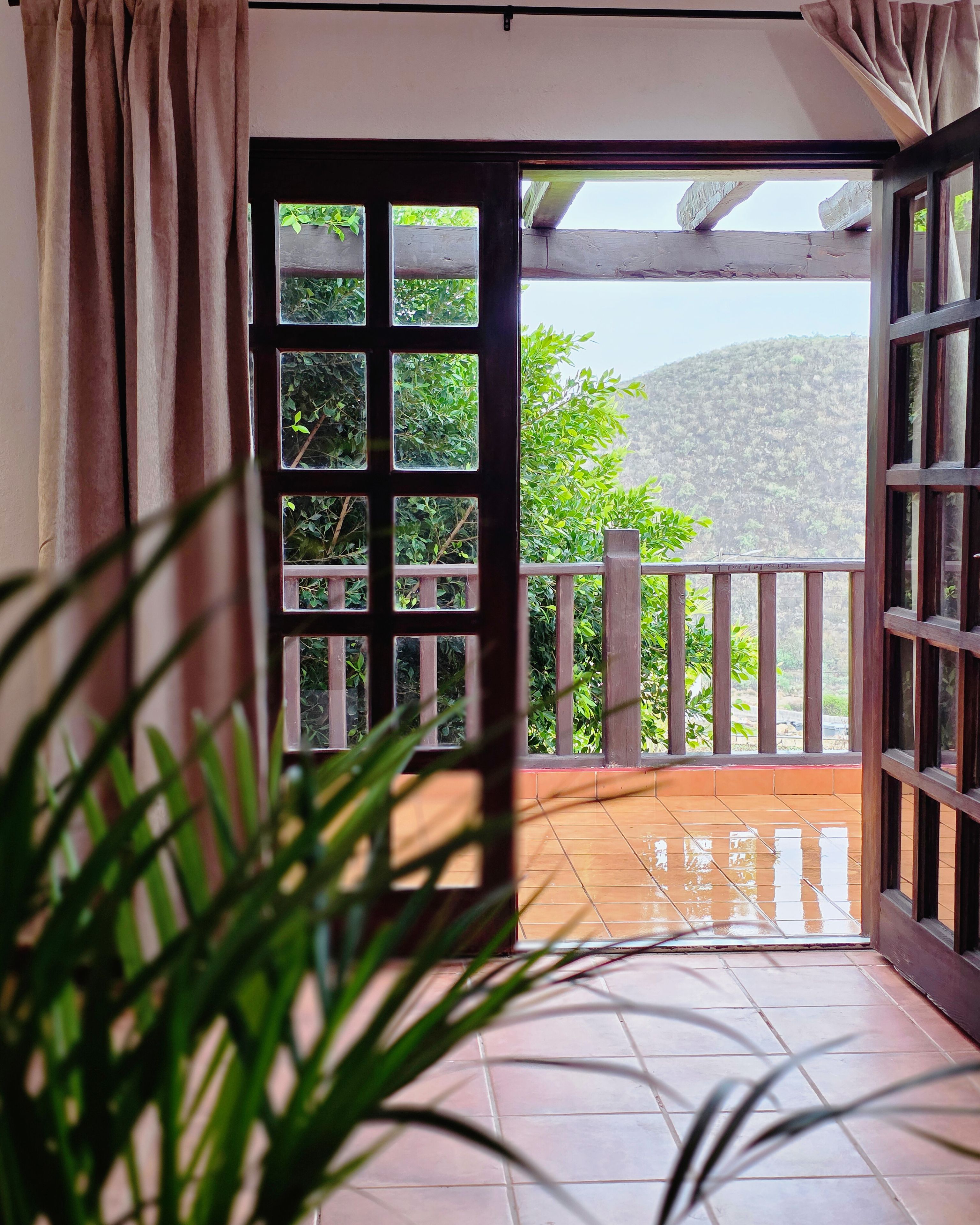 An open door leading to a balcony with a view of a hillside.