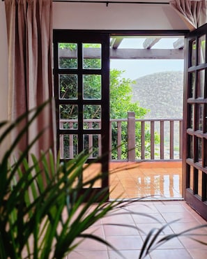 An open door leading to a balcony with a view of a hillside.