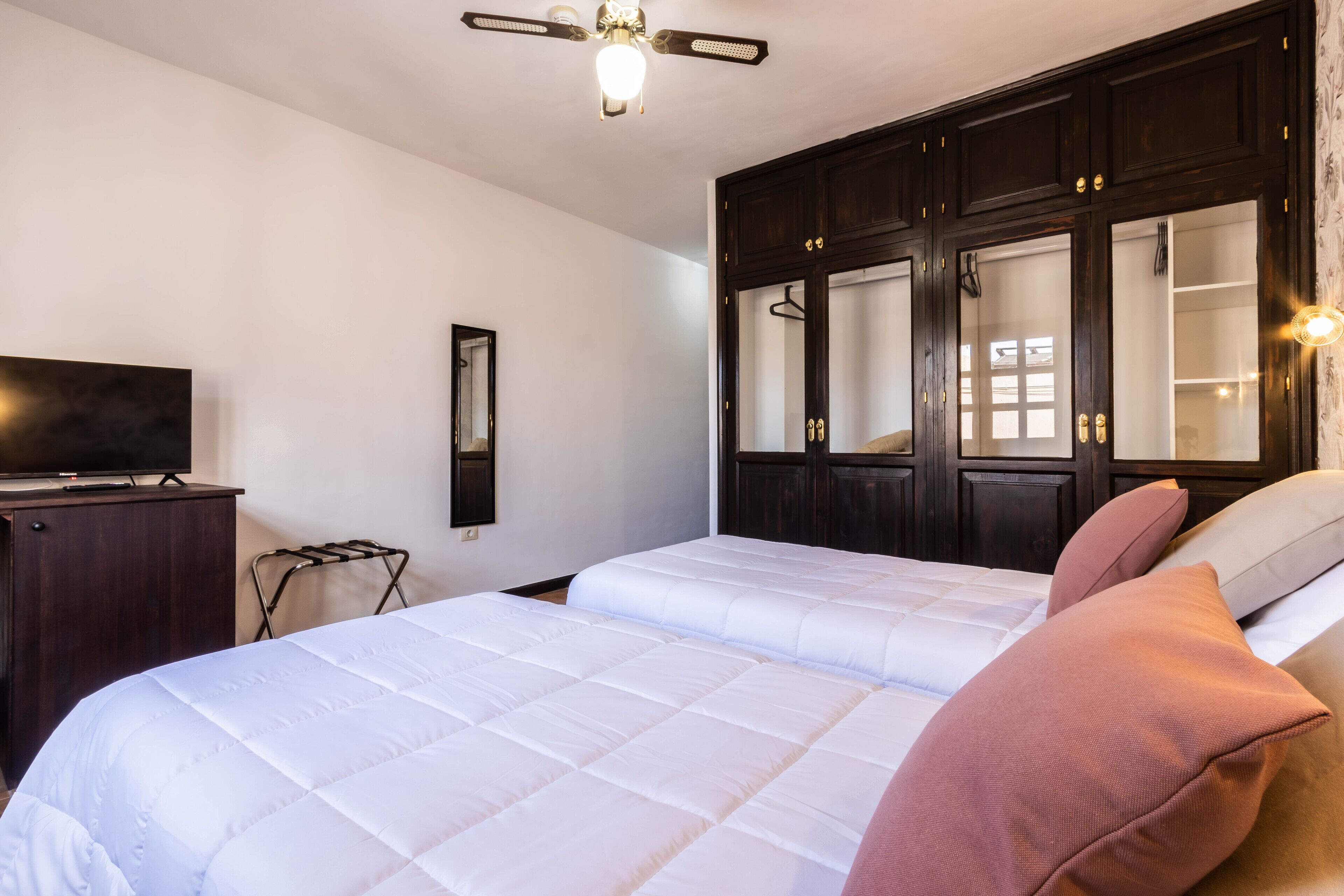 A hotel room with a bed, a TV on a dresser, a wardrobe, and a ceiling fan.