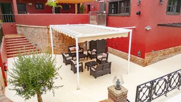 Une terrasse extérieure avec des meubles en osier, un espace salon couvert et un mur en pierre.