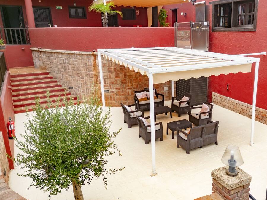 Une terrasse extérieure avec des meubles en osier, un espace salon couvert et un mur en pierre.