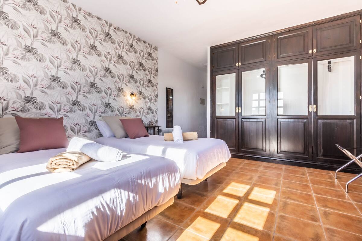 A hotel room with two beds, a large wardrobe, and a patterned wallpaper.
