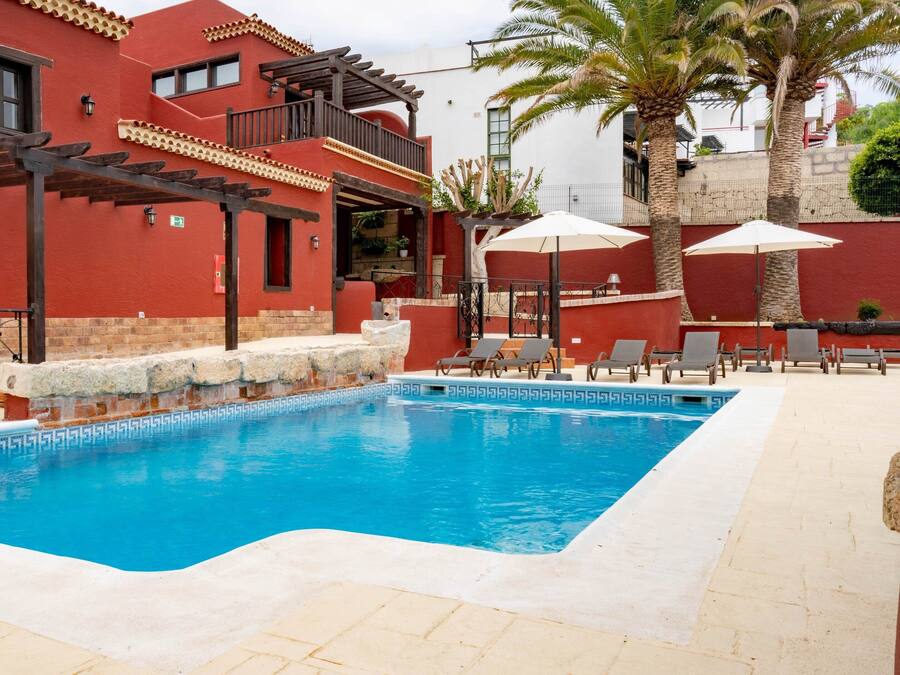Une piscine bordée de pierres, des chaises longues et un bâtiment rouge doté de balcons.