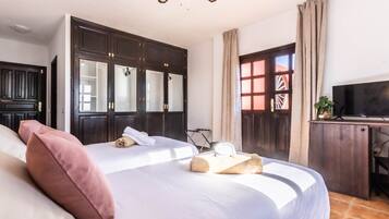 Un dormitorio con una cama grande, un armario de madera oscura, un escritorio con televisor y una ventana con cortinas.